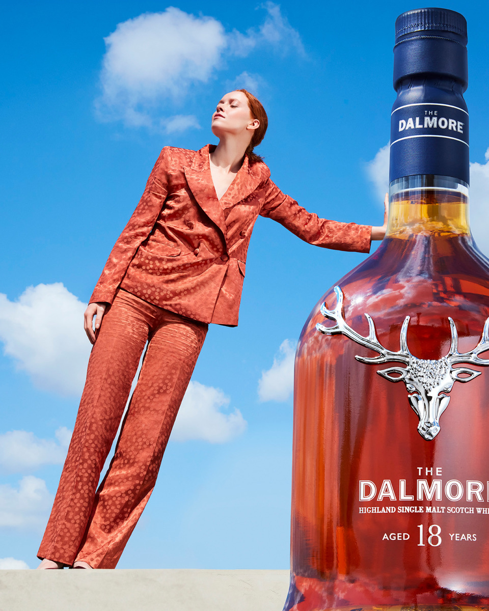 Woman leans on a bottle of whisky using perspective