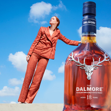 Woman leans on a bottle of whisky using perspective